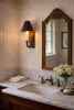 Traditional powder bathroom with marble countertop vanity, antique carved wood mirror, and brass wall sconce with dark shade