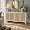 A white sideboard cabinet with four woven natural-fiber paneled doors, styled in a bright living room with a blue-and-white ceramic table lamp, a round mirror, and a large vase of white flowers.
